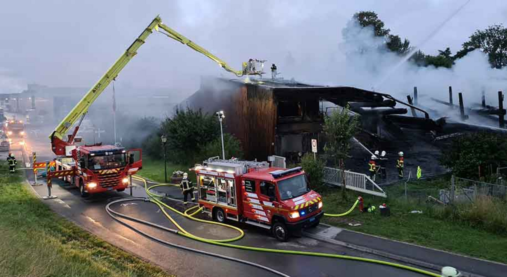 Mehrere Feuerwehrfahrzeuge stehen vor einem brennenden Haus