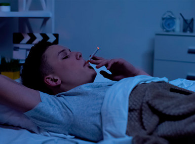 Ein Mann raucht im Bett eine Zigarrette