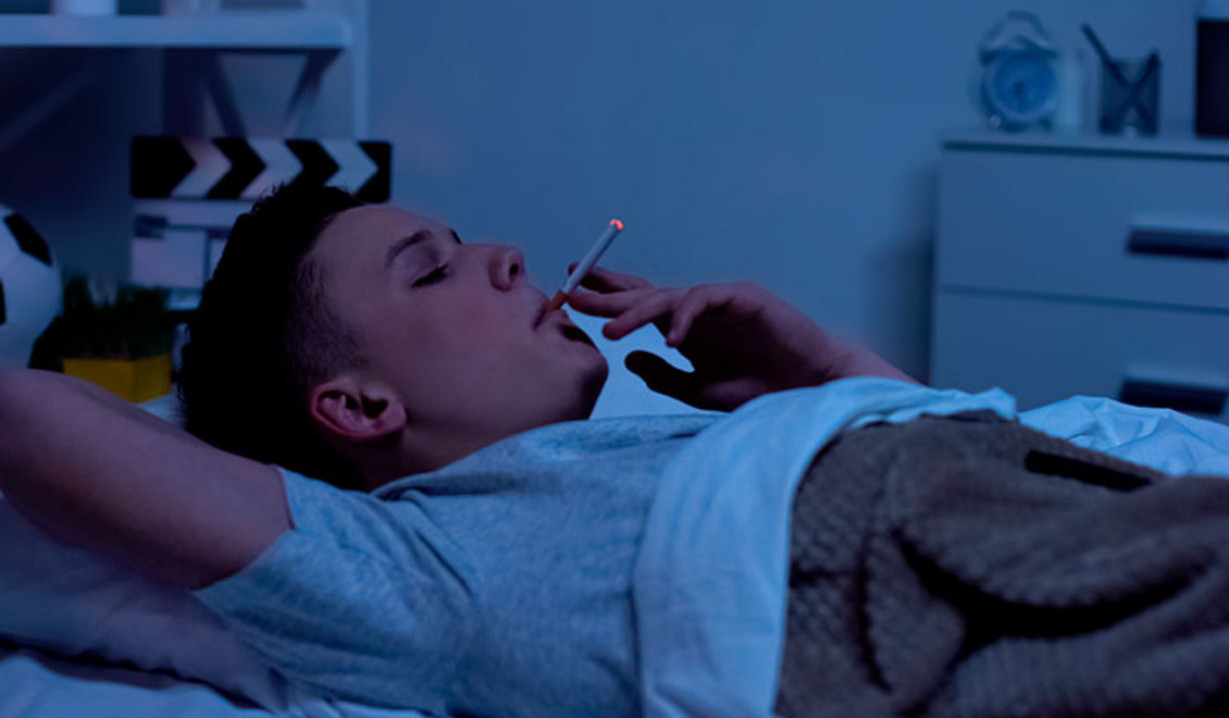 Ein rauchender Mann liegt im Bett