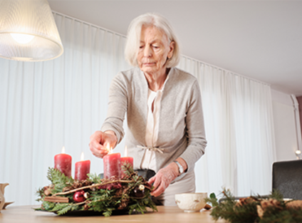 Une vieille femme allume une bougie sur la couronne de l'Avent