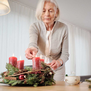 Une personne âgée allume les bougies de la couronne de l'Avent. 