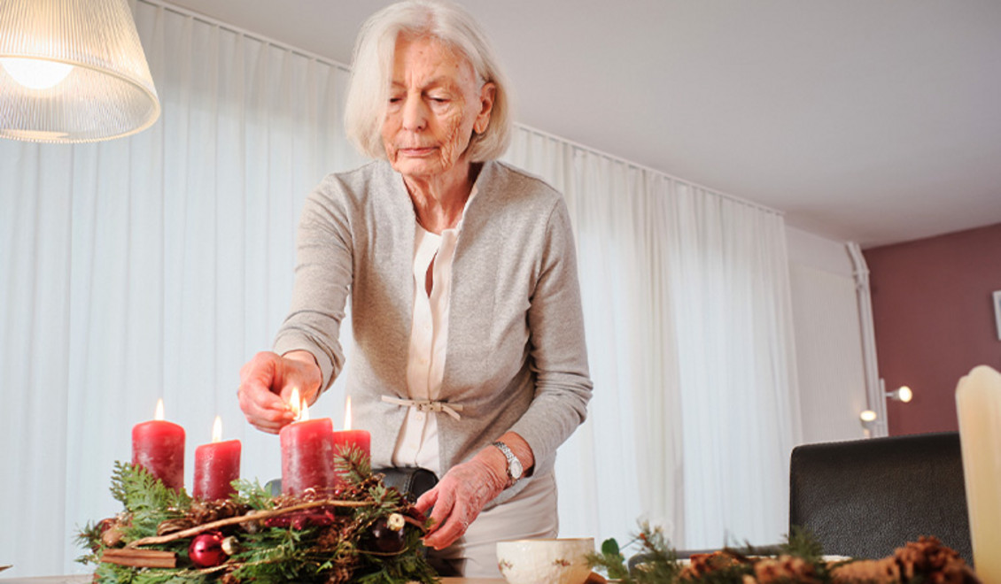 Une femme âgée allume une bougie sur la couronne de l'Avent.