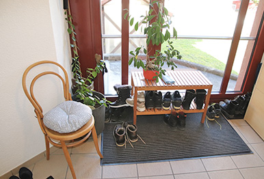 Ein Stuhl, ein Schuhmöbel, Pflanzen und Schuhe stehen im Treppenhaus. 
