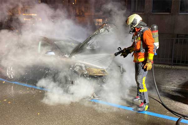 Ein Feuerwehrmann löscht das ausgebrannte Auto