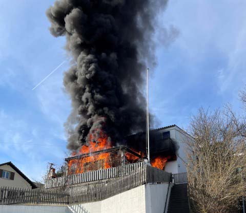 Schwarzer Rauch steigt auf aufgrund eines Feuers auf einer Terrasse vor einem Haus.