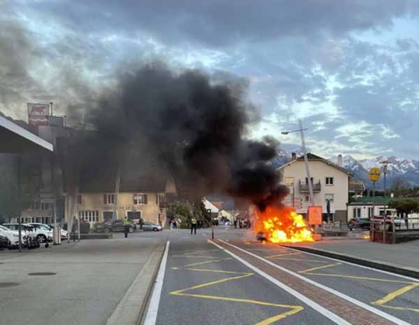Auf einer Strasse in der Mitte eines Ortzentrums brennt ein Auto licheterloh.