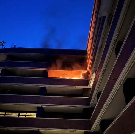 Auf einem Balkon eines Mehrfamilienhauses brennt es. Flammen und Rauch steigen auf.