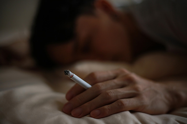Eine schlafende Person hält eine Zigarette in der Hand.