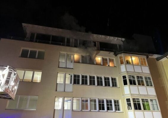Weisses Gebäude mit Fenster, aus denen Rauch rauskommt und man Feuer sieht.
