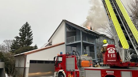 Ein weisses Haus und aus dem Dach kommt Rauch raus. Die Feuerwehr steht auf dem Platz.
