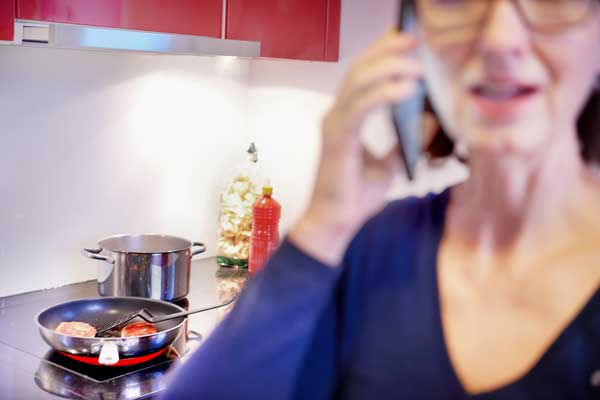 Frau erhält Anruf und lässt sich beim Kochen ablenken. 